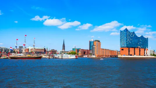 Blick auf die Hamburger Hafencity mit der Elbphilharmonie rechts im Bild, historischen Segelschiffen und Ausflugsschiffen im Vordergrund bei strahlend blauem Himmel