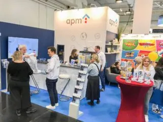 Messestand der apm mit mehreren Mitarbeitenden im Gespräch mit Besucherinnen und Besuchern; im Hintergrund ein hell gestalteter Stand mit Comic-Elementen, Broschürenständern, Monitor und Informationsmaterialien zum Thema Aus- und Weiterbildung in der Pflege